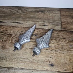 May include: Two silver metal finials with a textured surface. The finials have a pointed tip and a threaded base.