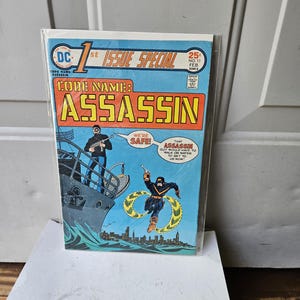 May include: A vintage comic book titled "1st Issue Special" featuring "Code Name: Assassin." The cover art depicts a man on a ship and another leaping over water. The comic has a blue, orange, and yellow color scheme.