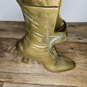 May include: A gold-colored metal boot-shaped vase. The boot has a high heel and a lace-up design.
