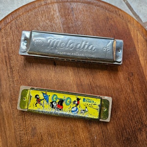 May include: Two harmonicas, one silver with the text "Melodia Made in Poland" and the other yellow with a cartoon image of children playing and the text "Star Made in China."