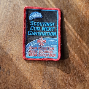 May include: A blue and red embroidered patch with the text "SCOUTING: OUR NEXT GENERATION" and "SAM HOUSTON AREA COUNCIL 1994 SCOUT FAIR".