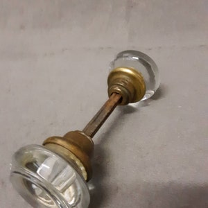 May include: A vintage glass door knob with a brass base and a metal rod. The knob is clear glass with a textured design.