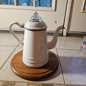 May include: White enamel coffee pot with a glass lid and a wooden base. The pot has a silver handle and spout.