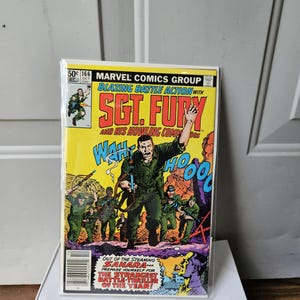 May include: A comic book cover for "Sgt. Fury and His Howling Commandos" features a yellow background with action-packed illustrations. The cover includes the text "Blazing Battle Action" and "Out of the Steaming Sahara... Prepare Yourself for The Strangest Battle-Thriller of the Year!"
