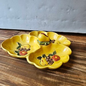May include: A yellow ceramic serving dish with four sections, each decorated with a different fruit design. The dish features pears, grapes, and apples in a stylized, hand-painted style.