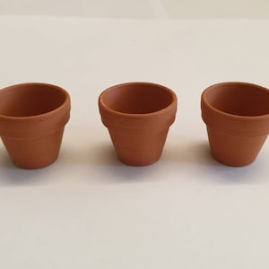 May include: Three terracotta flower pots, each with a round opening and a slightly flared rim. The pots are arranged in a row on a white surface.