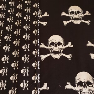 May include: Black fabric with a white skull and crossbones pattern. The fabric has a repeating pattern of skulls and crossbones on the left side and a larger skull and crossbones pattern on the right side.