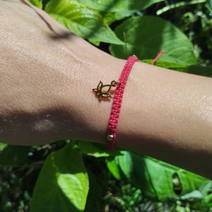 May include: A red string bracelet with a gold lotus charm. The bracelet is tied around a wrist.