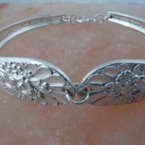 May include: A silver bracelet made from a vintage spoon with a floral design. The bracelet is open and has a clasp.