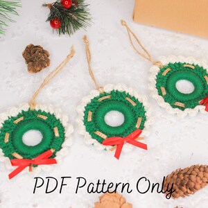 May include: Three crocheted Christmas wreaths made with white and green yarn, gold trim, and red bows. The wreaths are hanging from a white surface with pine cones and greenery. The text "PDF Pattern Only" is at the bottom of the image.