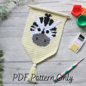 May include: A crochet wall hanging featuring a zebra face with black and white stripes. The hanging is made with a light yellow yarn and has a white tassel. The image also shows a crochet hook, yarn, and other craft supplies.