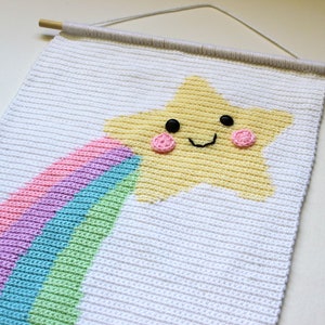 May include: A white crocheted wall hanging with a yellow star and a rainbow. The star has a smiling face with black eyes and pink cheeks.