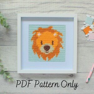 May include: A framed crochet pattern of a lion's face with orange, brown, and white yarn. The frame is white and the background is light blue. The text "PDF Pattern Only" is below the frame.