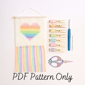 Peut inclure: Une suspension murale en crochet en forme de cœur arc-en-ciel avec une frange de fil coloré. Le kit comprend du fil, un crochet, des ciseaux et des pinces à linge en bois. Le texte "PDF Pattern Only" est en bas de l'image.