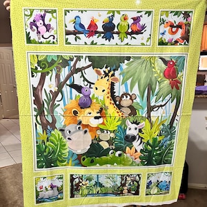 May include: A colorful fabric panel featuring a jungle scene with various animals. The design includes a giraffe, lion, monkey, zebra, and crocodile, surrounded by lush green foliage. Birds perch on branches, and the border is a light green with small dots.