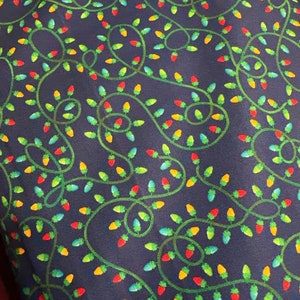 May include: A dark blue fabric with a repeating pattern of green, red, yellow, and blue Christmas lights. The lights are strung together in a festive design.