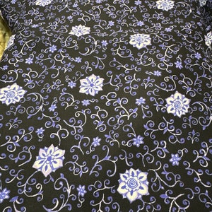 May include: Black fabric with a repeating pattern of white and blue stylized flowers and vines.