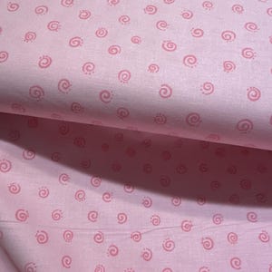 May include: Pink fabric with a repeating pattern of small pink swirls.