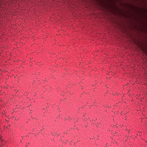 May include: Red fabric with a black floral pattern. The pattern is made up of small, delicate branches and leaves.