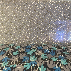May include: Two pieces of fabric with different patterns. The top fabric is light blue with a white bone pattern. The bottom fabric is dark gray with a light blue dinosaur footprint pattern.