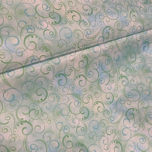 May include: Fabric with a repeating pattern of green and blue swirls and dots on a light blue and white background. The fabric is folded, showing the texture and layers of the material. The design is reminiscent of a watercolor painting.