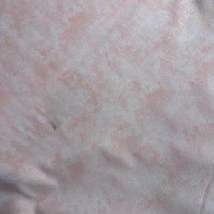 May include: A close-up of a soft, pink fabric with a subtle, marbled pattern. The fabric has a light, airy feel and a slightly textured surface.