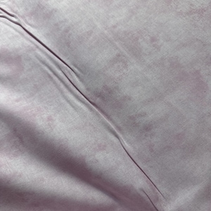 May include: A close-up of a light pink fabric with a subtle marbled pattern. The fabric has a soft, smooth texture and a slightly wrinkled appearance.