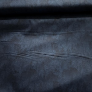 May include: Close-up of a dark blue fabric with a mottled texture. The material has subtle variations in color, creating a shadowed effect. The fabric appears soft and pliable, with gentle folds and creases.