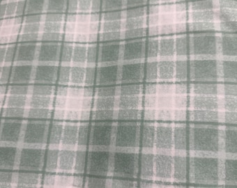 Könnte beinhalten: Ein Stoff mit einem weichen, salbeigrünen und weißen Karomuster. Das Design besteht aus sich kreuzenden horizontalen und vertikalen Linien unterschiedlicher Breite, die einen klassischen Gittereffekt auf der gesamten Oberfläche des Textils erzeugen.