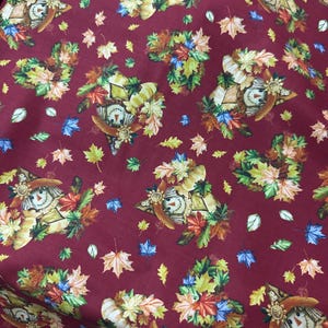 May include: A deep maroon fabric featuring a repeating pattern of scarecrows wearing straw hats, surrounded by clusters of colorful autumn leaves in shades of orange, yellow, green, and brown, interspersed with individual fallen maple leaves.