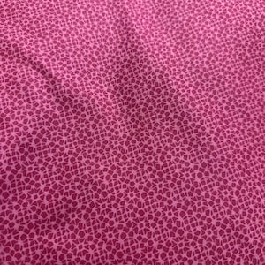 May include: Close-up of a pink fabric with a repeating pattern of small, irregular shapes. The pattern is a darker shade of pink than the background, creating a textured appearance. The fabric appears soft and pliable, with subtle folds and shadows.