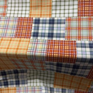 May include: A fabric featuring a patchwork design of various plaid patterns. The squares display a color palette of orange, navy blue, white, light blue, and green. The textile is composed of multiple rectangular sections stitched together.