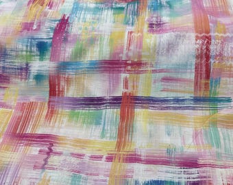 May include: A fabric with a colorful abstract design. The pattern features overlapping brushstrokes in shades of red, yellow, blue, purple, and green on a white background. The fabric appears to be folded.