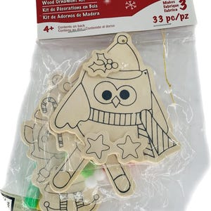Puede incluir: Un kit de adornos de madera Creatology con tres adornos de madera sin terminar en un paquete de plástico transparente. Los adornos incluyen un búho, un hombre de jengibre y un bastón de caramelo. El kit es para mayores de 4 años.