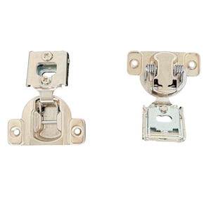 May include: Two silver-toned metal cabinet hinges with visible mounting plates and spring mechanisms. Each hinge features a rectangular base with two screw holes, a central pivot arm, and a circular cup attachment for installation into furniture.