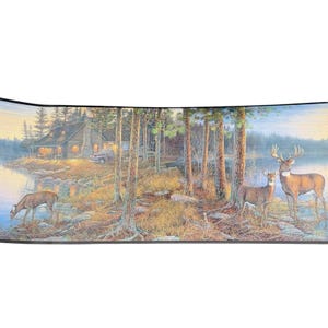 May include: A scenic landscape border featuring a cabin by a lake, deer, and trees. The artwork depicts a serene forest scene with a cabin, a truck, and deer in a natural setting. The color palette includes greens, browns, and blues.