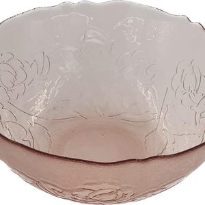May include: A light pink glass bowl with a scalloped rim. The bowl features an embossed floral design. The rim has a darker pink hue. The bowl is likely used for serving or display.