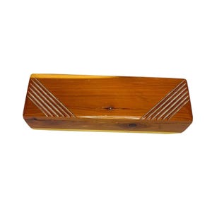 May include: A rectangular wooden box with a warm brown finish. The lid features diagonal carved lines at each end, adding a decorative touch. The box is likely used for storage or display of small items.