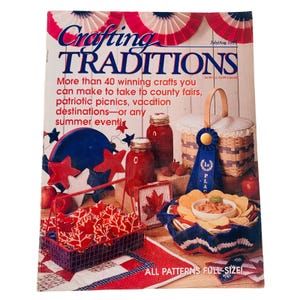 May include: A magazine cover with a red, white and blue patriotic theme. The cover text reads "Crafting Traditions" and "More than 40 winning crafts you can make to take to county fairs, patriotic picnics, vacation destinations - or any summer event!" The cover image features a variety of crafts, including a red, white and blue quilt, a basket of red and white cookies, a blue and white crocheted bowl, and a jar of red jelly.