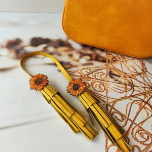 May include: A pair of yellow leather tassel earrings with sunflower accents. The earrings are handmade and feature a unique design.
