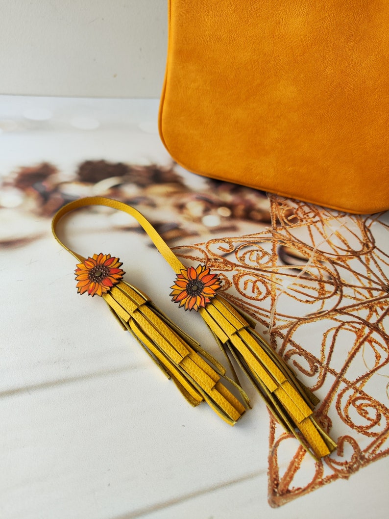 May include: A pair of yellow leather tassel earrings with sunflower accents. The earrings are handmade and feature a unique design.