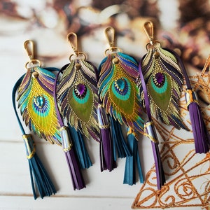 May include: Five colorful leather keychains shaped like peacock feathers with gold accents and purple and teal tassels.