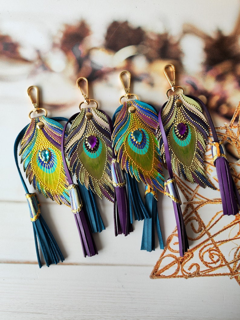 May include: Five colorful leather keychains shaped like peacock feathers with gold accents and purple and teal tassels.
