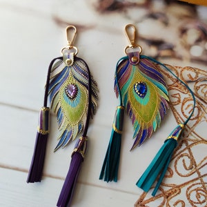 May include: Two peacock feather keychains with gold accents and jeweled eyes. One keychain has purple tassels and the other has teal tassels.