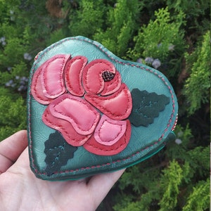 May include: A green leather heart-shaped coin purse with a pink and red leather rose appliqué. The rose has a beaded center and green leather leaves.