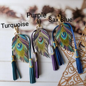 May include: Four peacock feather keychains with tassels. The feathers are made of leather and have a gold, green, blue, and purple color scheme. The tassels are in turquoise, purple, blue, and sax blue.