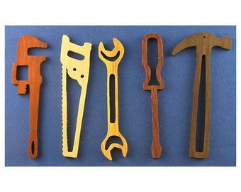 Op de afbeelding: Zes houten gereedschappen, waaronder een moersleutel, een zaag, een schroevendraaier, een hamer en een pijpsleutel, worden getoond tegen een blauwe achtergrond. De gereedschappen zijn allemaal van hout en hebben een natuurlijke afwerking.