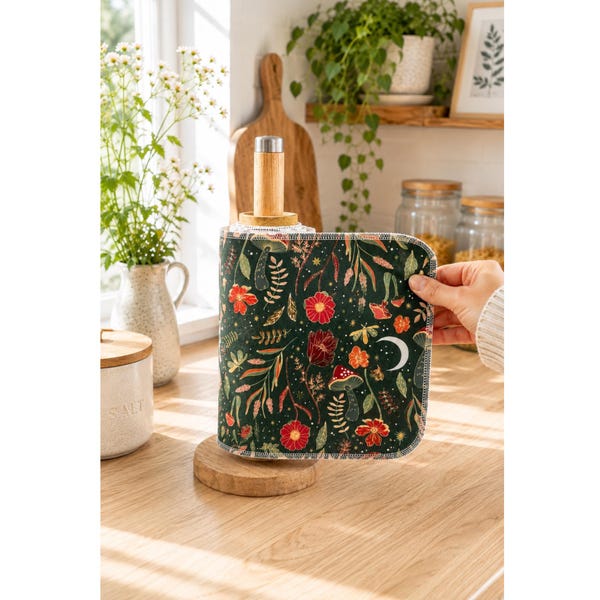 Può includere: Un foglio di carta da cucina riutilizzabile con sfondo verde scuro e una stampa botanica di fiori rossi, funghi, felci e una luna crescente bianca. Il foglio rettangolare in tessuto ha angoli arrotondati e bordi rifiniti con cuciture.