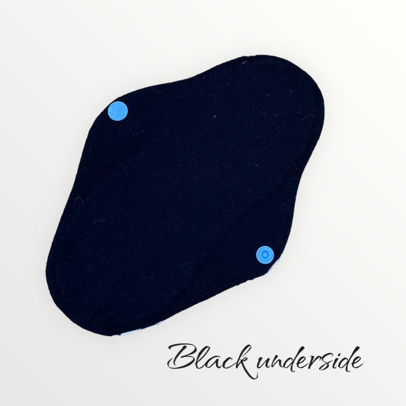 Może przedstawiać: Czarna wielorazowa podkładka z tkaniny z dwoma niebieskimi zatrzaskami. Pod podkładką napisano "Black underside".