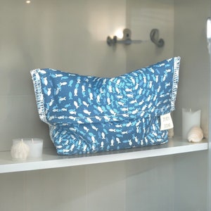 May include: A blue and white fabric storage bag with a fish pattern. The bag is folded and sitting on a white shelf. The bag has a small white tag with the text "DR. BECK" on it.